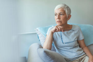 older woman sitting on couch and holding eyeglasses 
