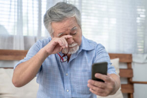 man holding phone and rubbing his eye