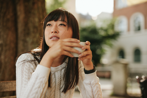 A woman holding a cup and curiously gazing to her side