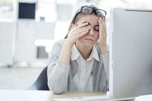 woman sitting at desk and rubbing her dry eye